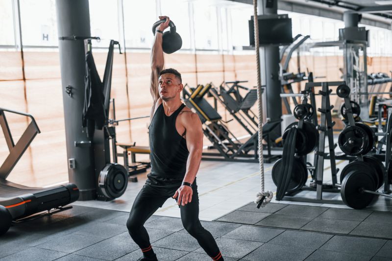 A person practicing the correct Single Arm Snatch with a kettlebell at a Fitness4Less gym to build full-body strength.